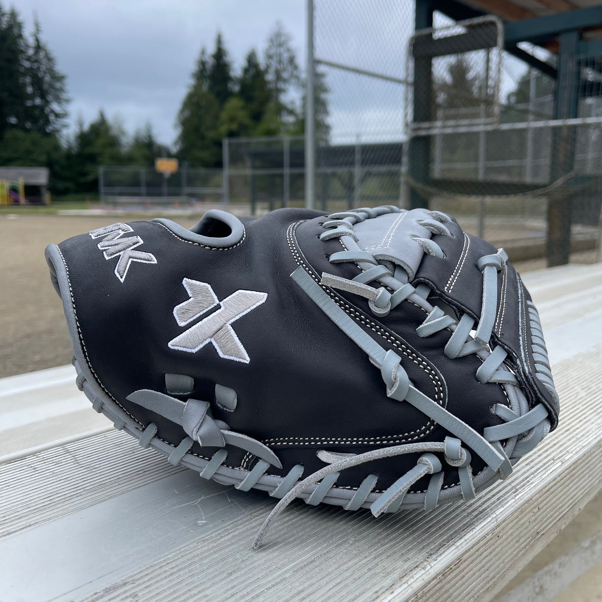 Black and gray baseball glove with 'KTMK' logo on a wooden surface, field background