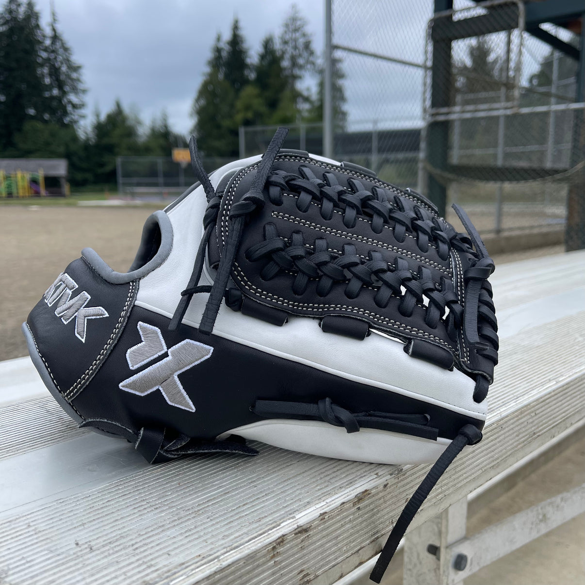 Black and white softball glove on a wooden bench with a sports field background