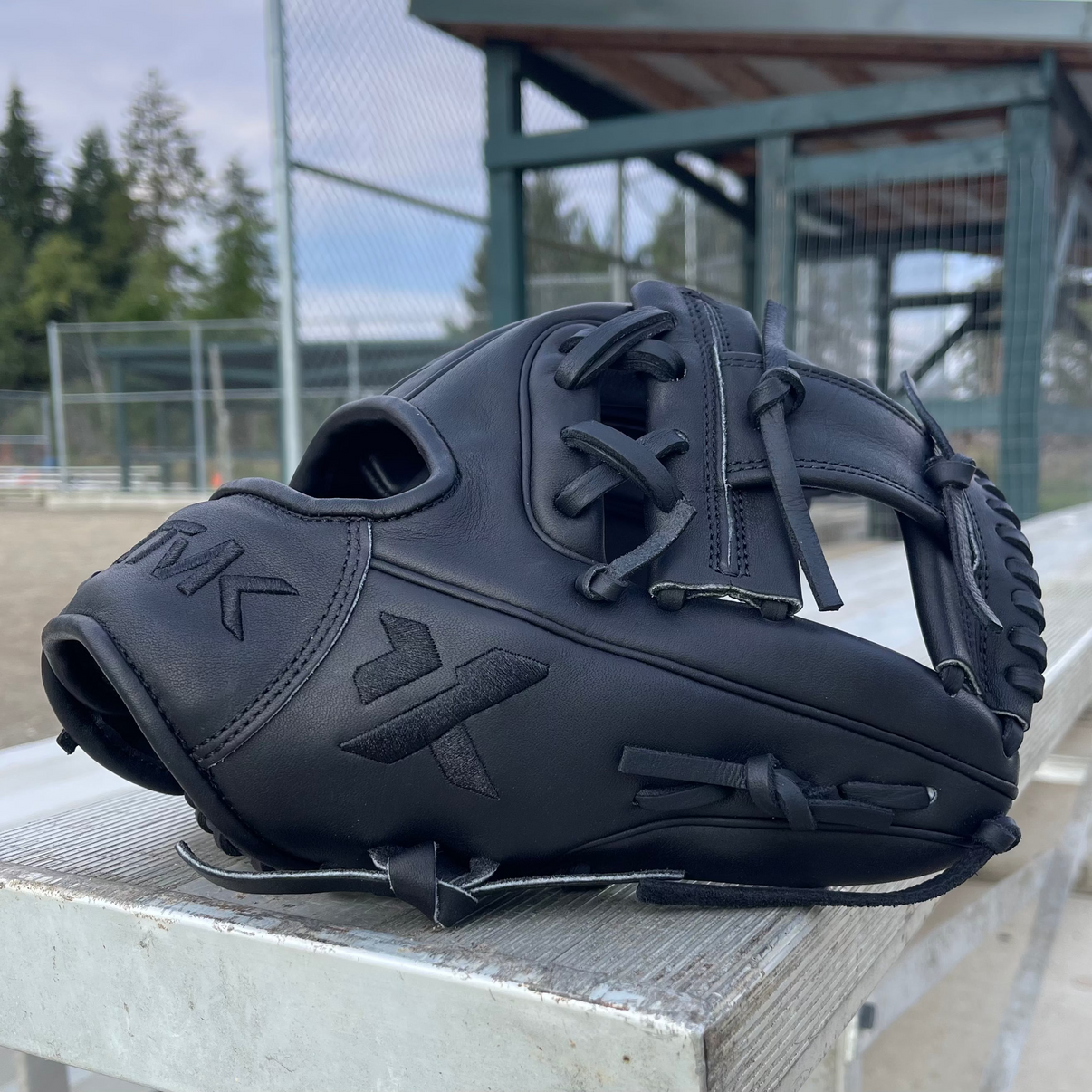Black baseball glove with 'KTMK' branding on a metal surface outdoors.
