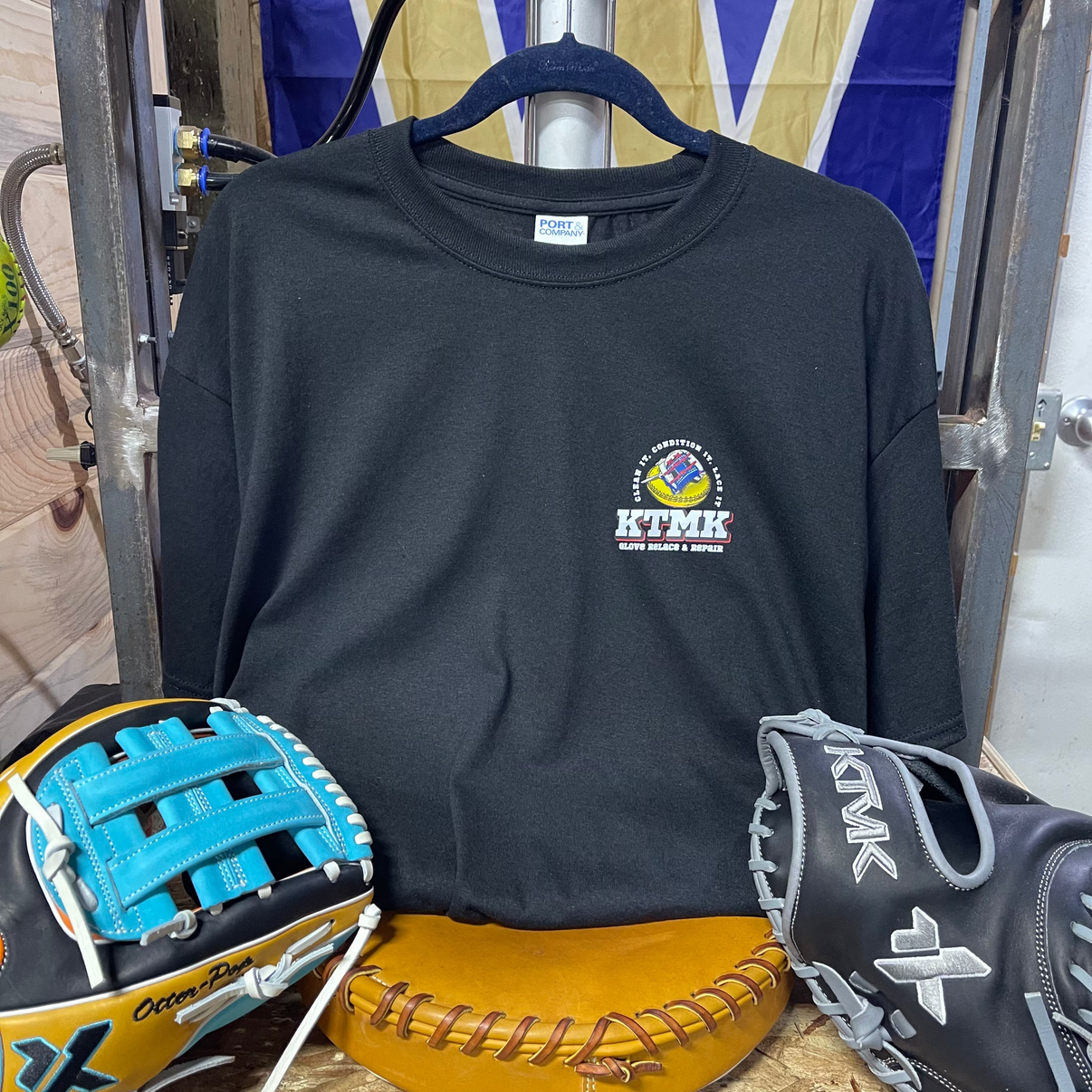 Black long-sleeve shirt with a logo, two baseball gloves, and a sports ball on a wooden surface.